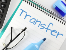 Block mit Schrift "Transfer" in hellblau, Anschnitt eines Taschenrechners, einer Brille und eines hellblauen Textmarkers